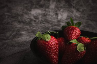 Taze kırmızı çilekler kasede. Koyu taş masa üzerindeki çilek meyveleri metin için fotokopi alanı. en üstteki görünüm.