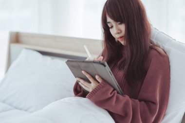 Beyaz bir yatak odasında tablet çalan bir kadın.