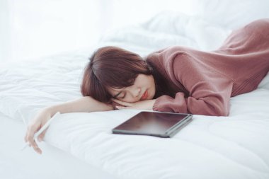 Beyaz bir yatak odasında tablet çalan bir kadın.