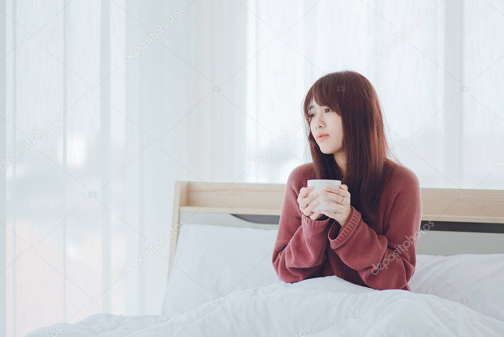 Woman holding a cup (coffee, tea, milk) on the bed in a white room,Woman drinking (coffee, tea, milk)