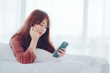 Evdeki yatakta telefonla oynayan bir kadın.