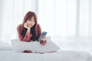 Evdeki yatakta telefonla oynayan bir kadın.