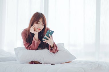 Evdeki yatakta telefonla oynayan bir kadın.