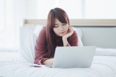 Dizüstü bilgisayarda çalışan bir kadın evdeki yatakta oturuyor..