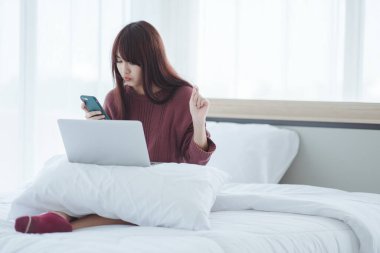 Dizüstü bilgisayarda çalışan bir kadın evdeki yatakta oturuyor..