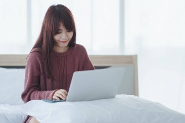 Dizüstü bilgisayarda çalışan bir kadın evdeki yatakta oturuyor..