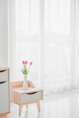 Yatak odasında, yatak odasında saat ve vazo bulunan modern yatak odası ve yatak odası dolabını kapat. Komodinin üzerinde buket var.