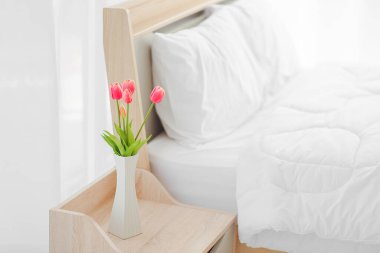 Yatak odasında, yatak odasında saat ve vazo bulunan modern yatak odası ve yatak odası dolabını kapat. Komodinin üzerinde buket var.