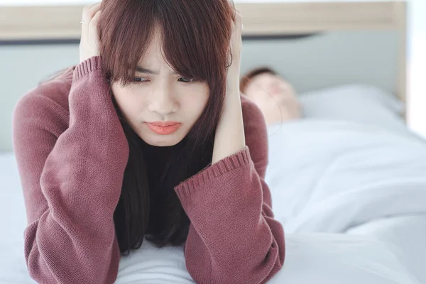 couple in bed man sleeps and snores while woman is unable to sleep closing her ears with big pillows,woman blocking ears with pillow while man snoring on bed