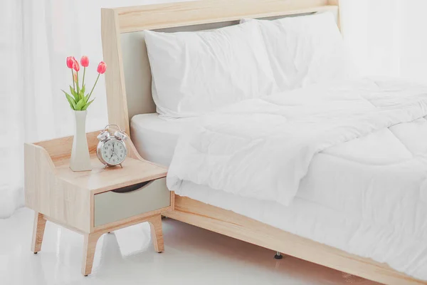 Close up of modern bed and bedside cabinet with clock and flower vase in the bedroom,bedroom. bouquet on the nightstand