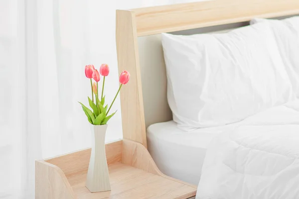 Close up of modern bed and bedside cabinet with clock and flower vase in the bedroom,bedroom. bouquet on the nightstand