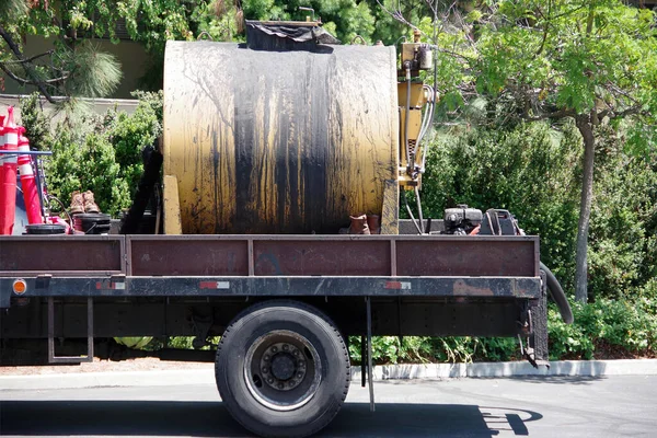 Back part of a construction truck with a big yellow tank for asphalt slurry seal