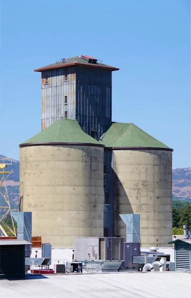 Backside view of a feed and grain silo and warehouse next to a California river and old train line with blue sky above