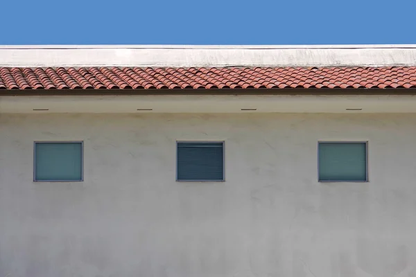 青い空の下に白い瓦の屋根の建物の上部に3つの窓があります — ストック写真