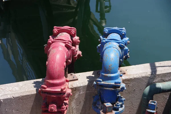 Close-up view of two main water lines marked red and blue at a fishing harbor retainer wall with reflecting water behind