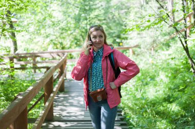 Bir kadın bir turist ceket ve bir orman parkta telefonda konuşurken bir sırt çantası. Yaz güneşli gün