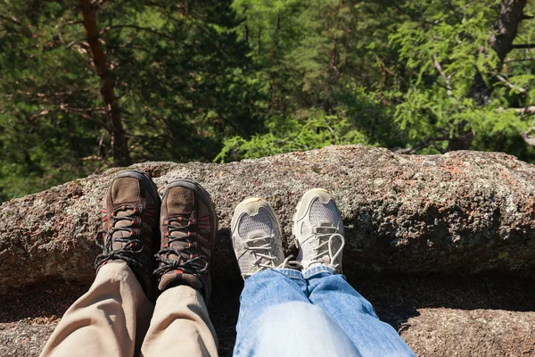 He and she rest. Two pairs of feet in sport shoes stick out on the rock. Adventures for Two