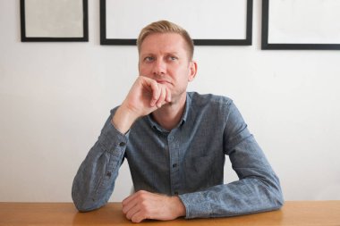 Adam düşünüyor. Gri gömlekli bir adam gri bir arka plan üzerinde bir masada oturuyor