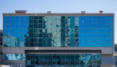 Architecture and blue sky are reflected in the glass wall of a rectangular building. Theme of modern geometric architecture and urbanization clipart
