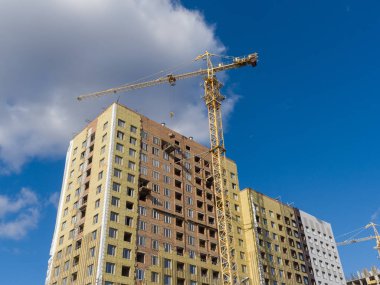 Bir vinç, yüksek katlı bir tuğla bina inşa ediyor. Duvarlar izole edilmiş. İnşaat halindeki gelişmekte olan bir konut piyasasının teması