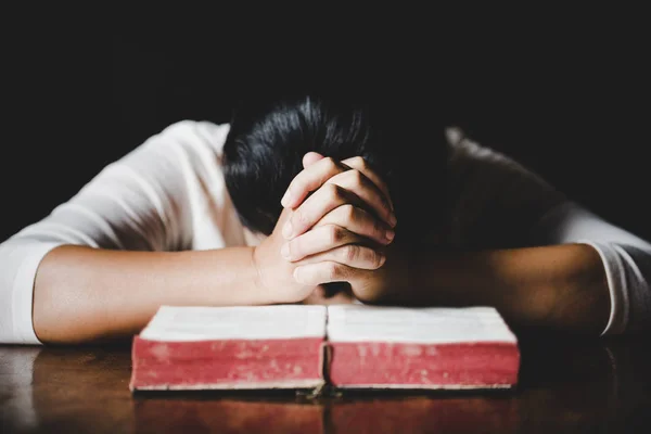 Woman hands praying with a bible in a dark over wooden table