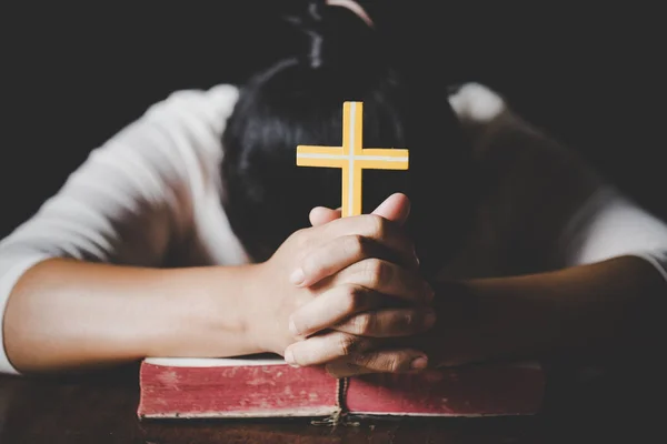 Woman hands praying with a cross and bible in a dark over wooden table