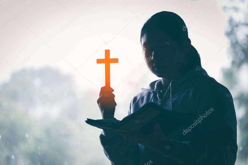 Teenager woman hand with Cross and Bible praying, Hands folded in prayer on a Holy Bible in church concept for faith, spirituality and religion.