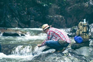 Genç uzun yürüyüşe çıkan kimse dağda akış su içme. Susuz turist hevesle bir şelale bir dağ nehir üzerinde gelen suyu içer.