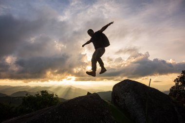 Siluet özgürlük-genç adam günbatımında iki rocky dağları arasındaki uçurumun atlıyor.