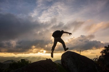 Siluet özgürlük-genç adam günbatımında iki rocky dağları arasındaki uçurumun atlıyor.