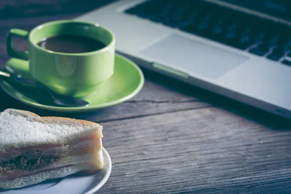 Cup of coffee and sandwich with a laptop on wooden table
