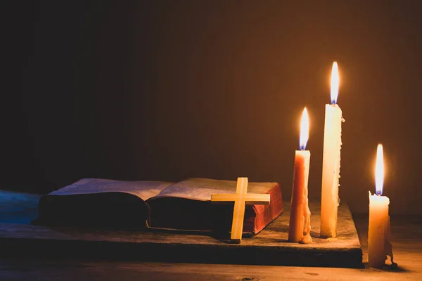 Cross with bible and candle on a old oak wooden table. Beautiful gold background. Religion concept.