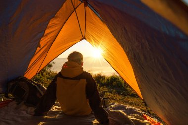 Kışın dağ manzaraya bakarak çadırda oturan bir genç adam. Işık efektleri