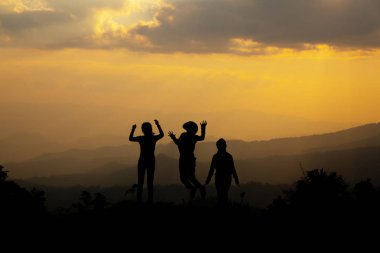 Gün batımında, tepede eğleniyor hakkında kavram dağın içinde atlama mutlu insanların grup, siluet 