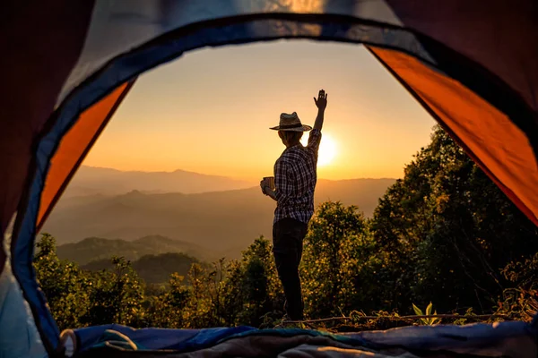 レジャーと自由を楽しんでいる夕日の光空の下山地周辺テント近くでコーヒー カップ滞在を保持するいると幸せな男 — ストック写真