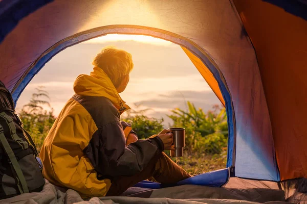 若い男とコーヒー カップを保持しているテントに座って冬の山の風景を見ています 光の効果 — ストック写真