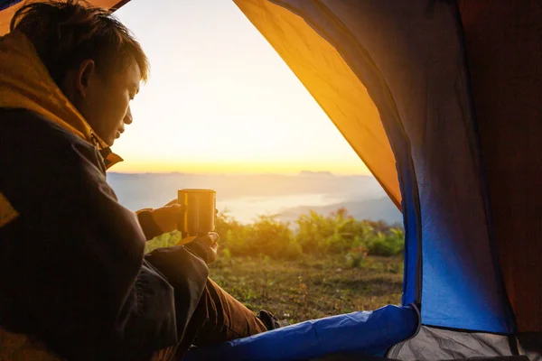若い男とコーヒー カップを保持しているテントに座って冬の山の風景を見ています 光の効果 — ストック写真