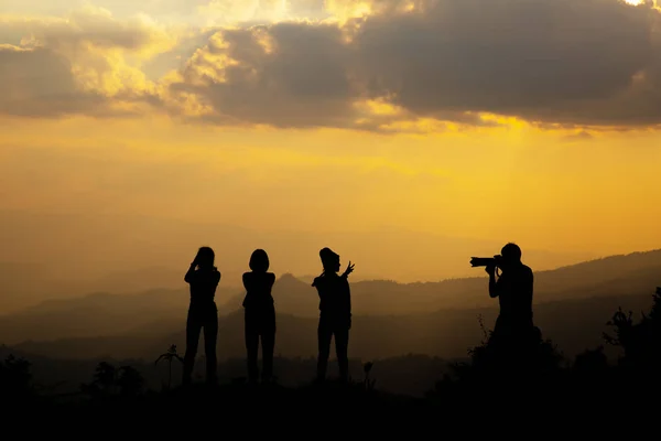 Group of happy people photographing in the mountain at sunset, concept about having fun on the hill, silhouette