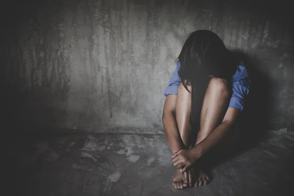 Üzgün küçük kız umutsuzluk içinde duvara karşı oturan.