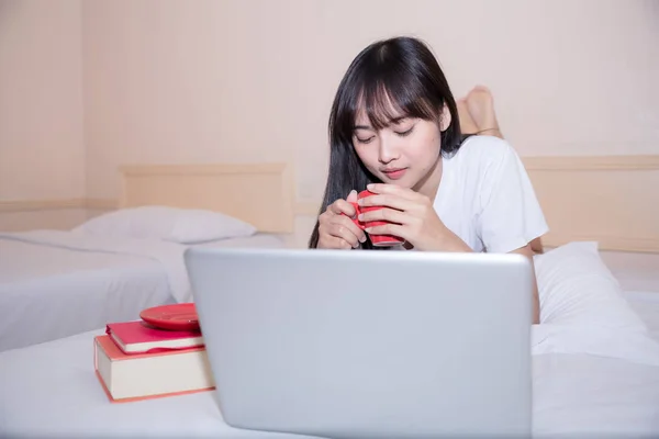 Розслаблена молода жінка сидить на ліжку з чашкою кави — стокове фото