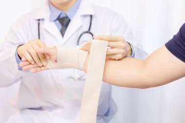 Erkek doktor klinikte genç adamın eline gazlı bez koyarak.