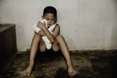 İhmal edilmiş yalnız çocuk, yerde elinde fotokopi uzayı olan bir bebekle oturan çocuk..