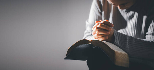 Hands folded in prayer on holy bible in church concept for faith, spirituality and religion. Unrecognizable woman holding a bible in her hands and praying. Hands clasped in prayer over holy bible.