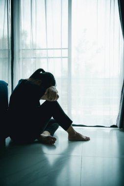 Yalnız bir kadın karanlık odada elleri başının üstünde pencere kenarında oturur. Depresyon, üzüntü, endişe, stres, zihinsel sağlık sorunu, yalnızlık ve duygusal mücadele kavramı.
