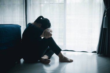 Üzgün bir kadın karanlık bir odada yerde oturuyor. Başı pencerenin yanında dinleniyor. Depresyon, stres, endişe, yalnızlık, akıl sağlığı sorunu, duygusal mücadele ve psikolojik sorun kavramı.