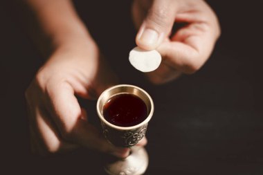 Ahşap bir kâse ve şarap kadehiyle komünyon ekmeğini tutan eller, Kutsal Komünyonu, Ayini, İsa 'nın kurban edilmesini ve Hristiyan inancının Lord Supper' a olan bağlılığını simgeliyor..