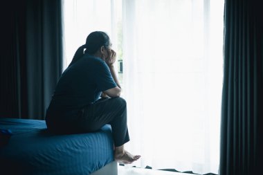 Yatakta yalnız başına oturan bir kadın karanlık odada pencereye bakar, depresyonu, yalnızlığı, endişeyi, üzüntüyü, zihinsel sağlık mücadelesini, uykusuzluğu ve hayattaki duygusal stresi simgeler..