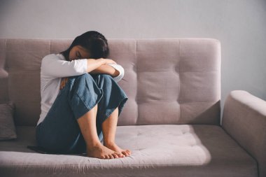Depresyondaki kadın kanepeye oturur. Kederli insan yalnız başına oturur ve dizlerine sarılır sıkıcı üzgün üzgün sinirli sinirli. Boğucu bir yük altında umut bulmak için mücadele ediyorlar. ruh sağlığı kavramı.
