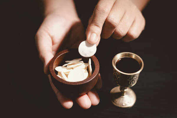 Руки, держащие хлеб причастия с деревянной чашей и чашей вина, символизирующие Святое Причастие, Евхаристию, жертву Иисуса Христа и христианскую веру в Вечерю Господню.