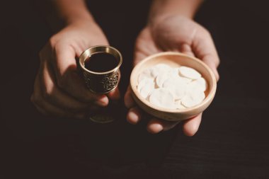 Ahşap bir kâse ve şarap kadehiyle komünyon ekmeğini tutan eller, Kutsal Komünyonu, Ayini, İsa 'nın kurban edilmesini ve Hristiyan inancının Lord Supper' a olan bağlılığını simgeliyor..